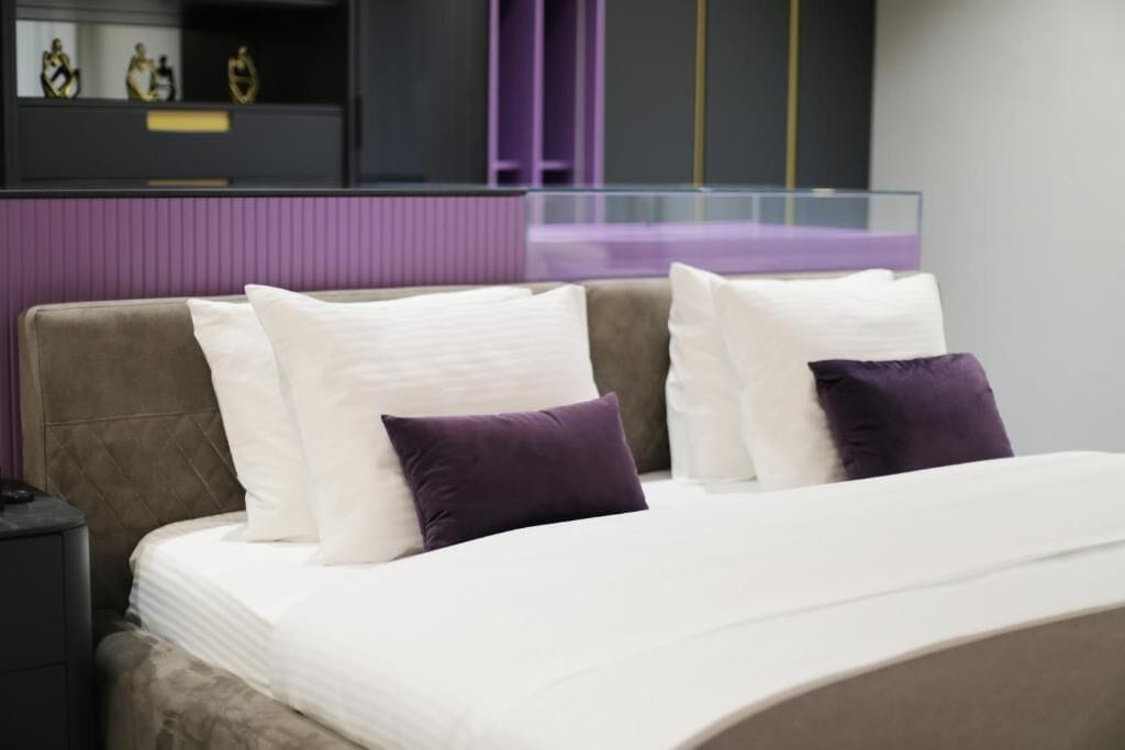 A bed with white and purple pillows, a headboard, and a nightstand.