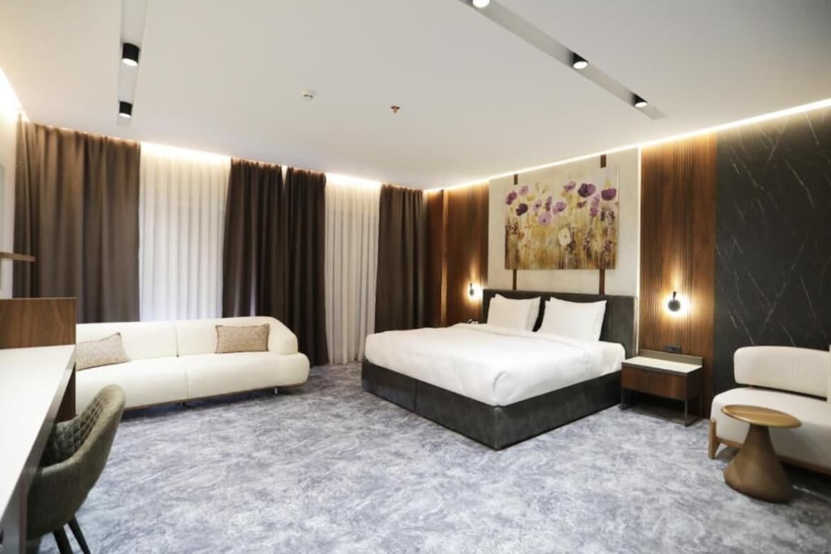 A modern hotel room with a large bed, a sofa, a desk, and a small table.