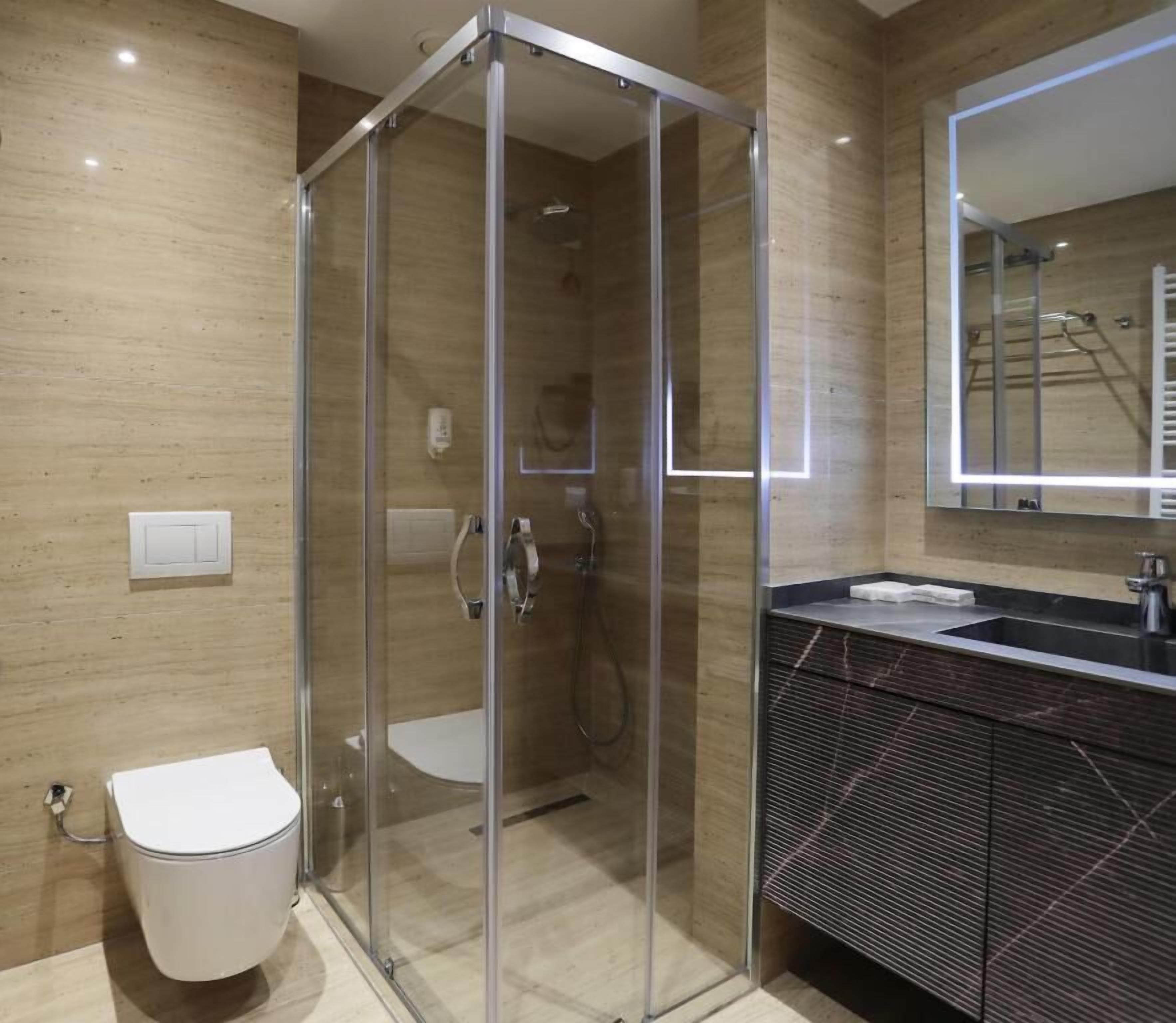 Un baño moderno con ducha envuelta en cristal, inodoro y tocador con espejo.