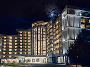 A multi-story hotel with a prominent entrance labeled 'HOTEL GALLERY,' featuring a modern architectural design with large windows and a symmetrical facade. - Hotel Gallery  (Gjilan)