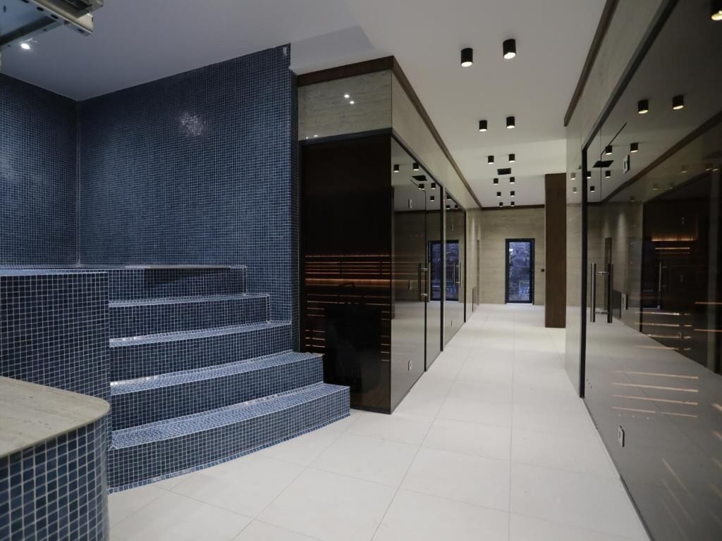 A modern hotel corridor with a tiled wall, a staircase, and a glass partition.