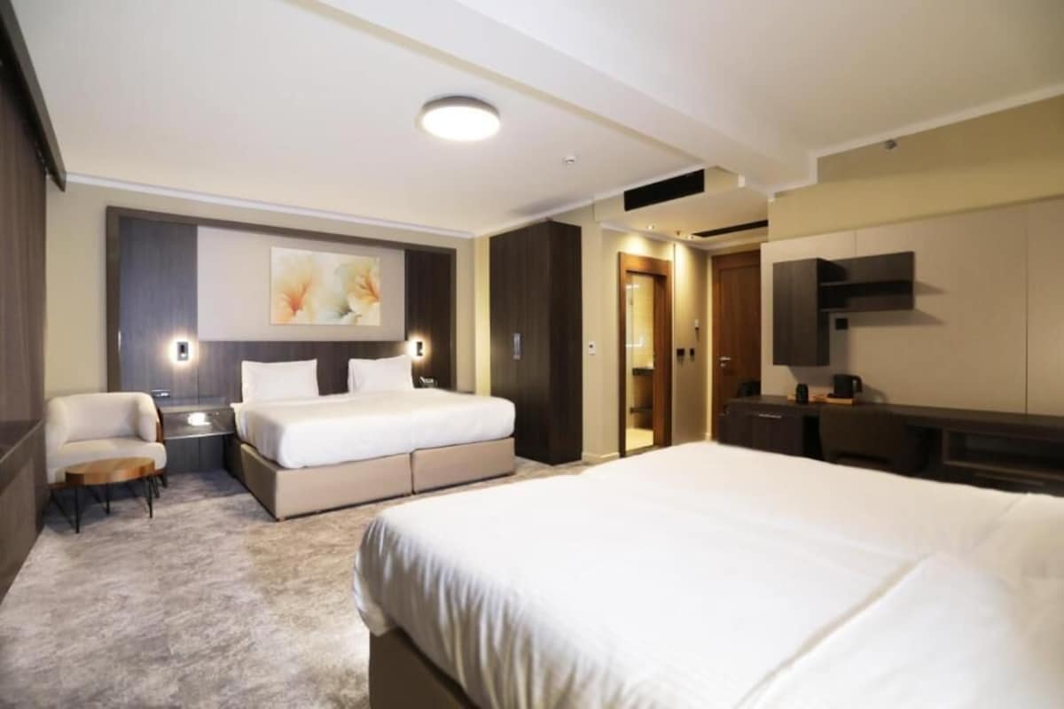 A hotel room with a large bed, a desk, a chair, and a wardrobe.