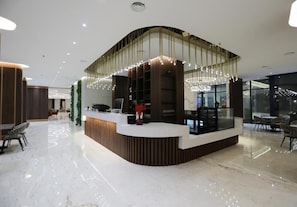 A modern reception area with a curved counter, a seating area with chairs, and a glass partition. - Hotel Gallery  (Gjilan)
