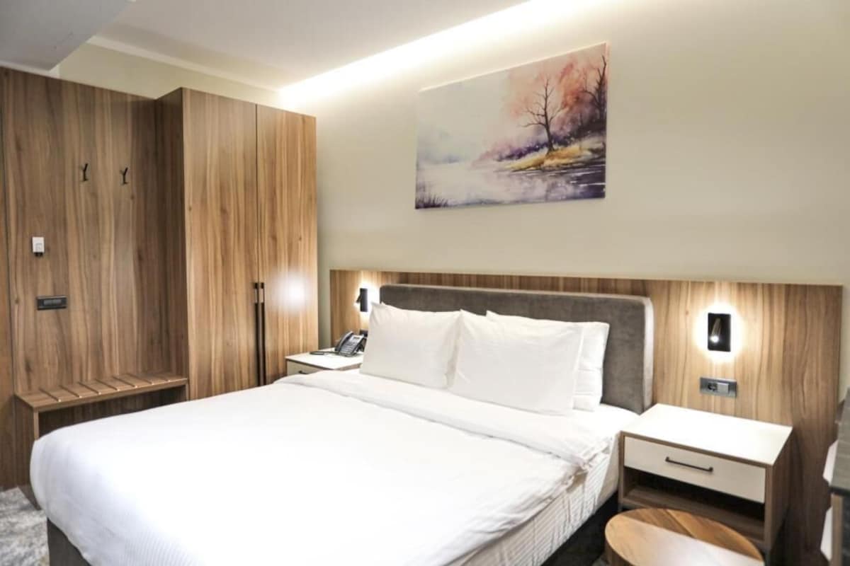 A hotel room with a large bed, wooden wardrobe, bedside tables, and a painting on the wall.