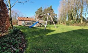 Ein grünes Hinterhof mit einer Holzschaukel und einer blauen Rutsche.