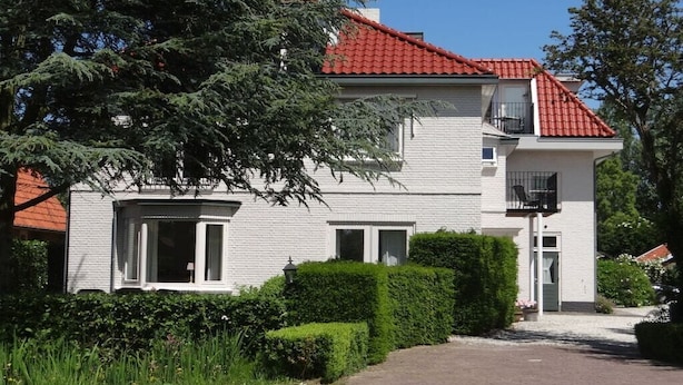 A two-story house with a red-tiled roof, white exterior walls, and a front entrance with a small porch. - Holiday apartment with 1 bedroom (oostkapelle)