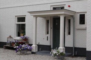 Ein weißes Gebäude mit schwarzem Türrahmen, einer kleinen Veranda und Blumentöpfen auf dem Boden.