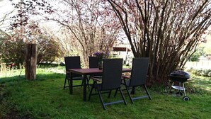 Ein Essbereich im Freien mit Tisch und Stühlen, umgeben von Gras und Bäumen.