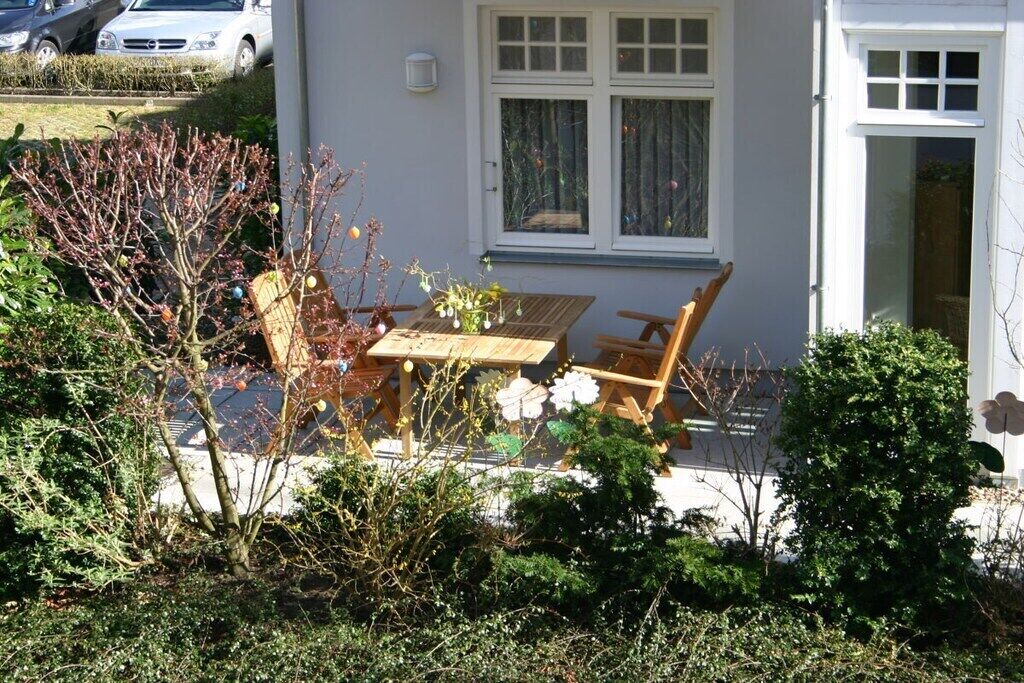 Il s’agit d’une propriété résidentielle dotée d’un patio comprenant une table et des chaises en bois, le tout entouré de divers arbustes et d’un petit arbre.