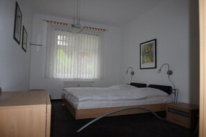 A bedroom with a bed, a desk, a radiator, and a window with curtains. - Holiday apartment with 2 bedrooms (Kühlungsborn)