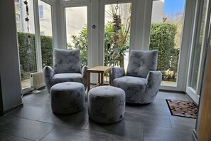 A room with a modern design, featuring a seating area with two armchairs and a ottoman, a small wooden table, and a view of the outdoors through large windows. - Holiday apartment with 2 bedrooms (Kühlungsborn)