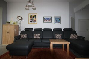 A living room with a black sectional sofa, a wooden coffee table, and a red rug. There are three framed artworks on the wall and a cabinet with decorative items. - Holiday apartment with 2 bedrooms (Kühlungsborn)