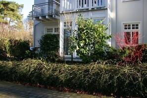 A two-story building with a balcony, surrounded by dense shrubbery and trees. - Holiday apartment with 2 bedrooms (Kühlungsborn)
