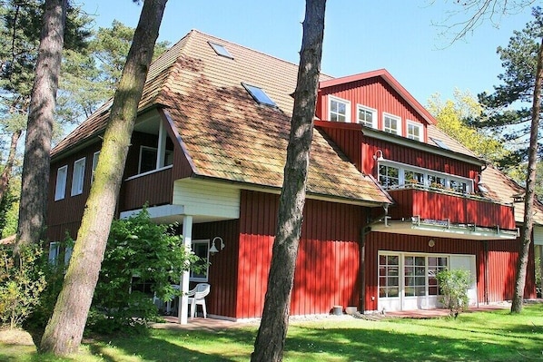 Een rood gebouw met twee verdiepingen, een schuin dak, een overdekte veranda en een garage.