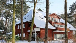 Una casa de fusta de dos pisos amb un teulat cobert de neu, envoltada d'arbres.