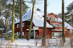Een houten huis met twee verdiepingen en een met sneeuw bedekte kap, omringd door bomen.