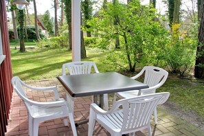 Een buitenpatio met een tafel en vier stoelen, omringd door groen en bomen.