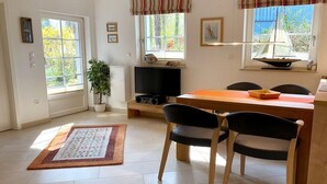 Habitació amb taula de dinar, cadires, televisió, planta en test i finestra amb model de veler.