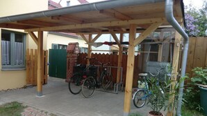 A covered outdoor area with a wooden structure, bicycles, and potted plants. - Holiday apartment with 1 bedroom (Potsdam)