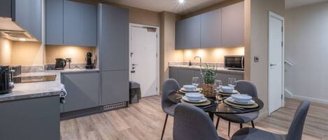A modern kitchen with grey cabinets, a dining table set for four, and a microwave.