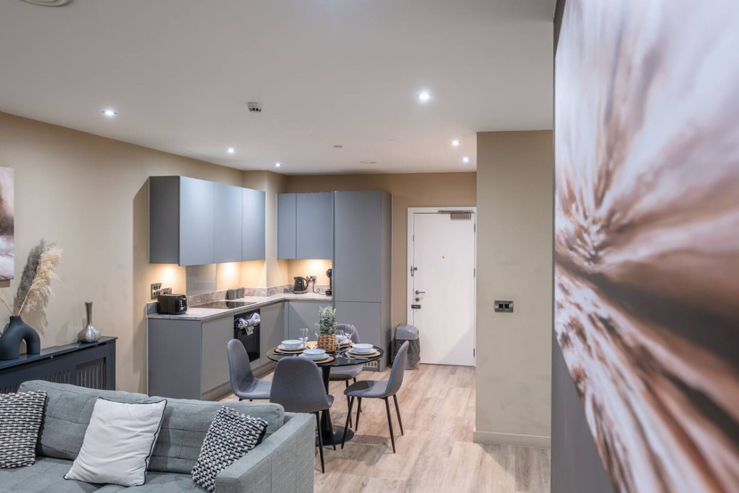 A modern living room with a grey sofa and a dining area with a table set for four.