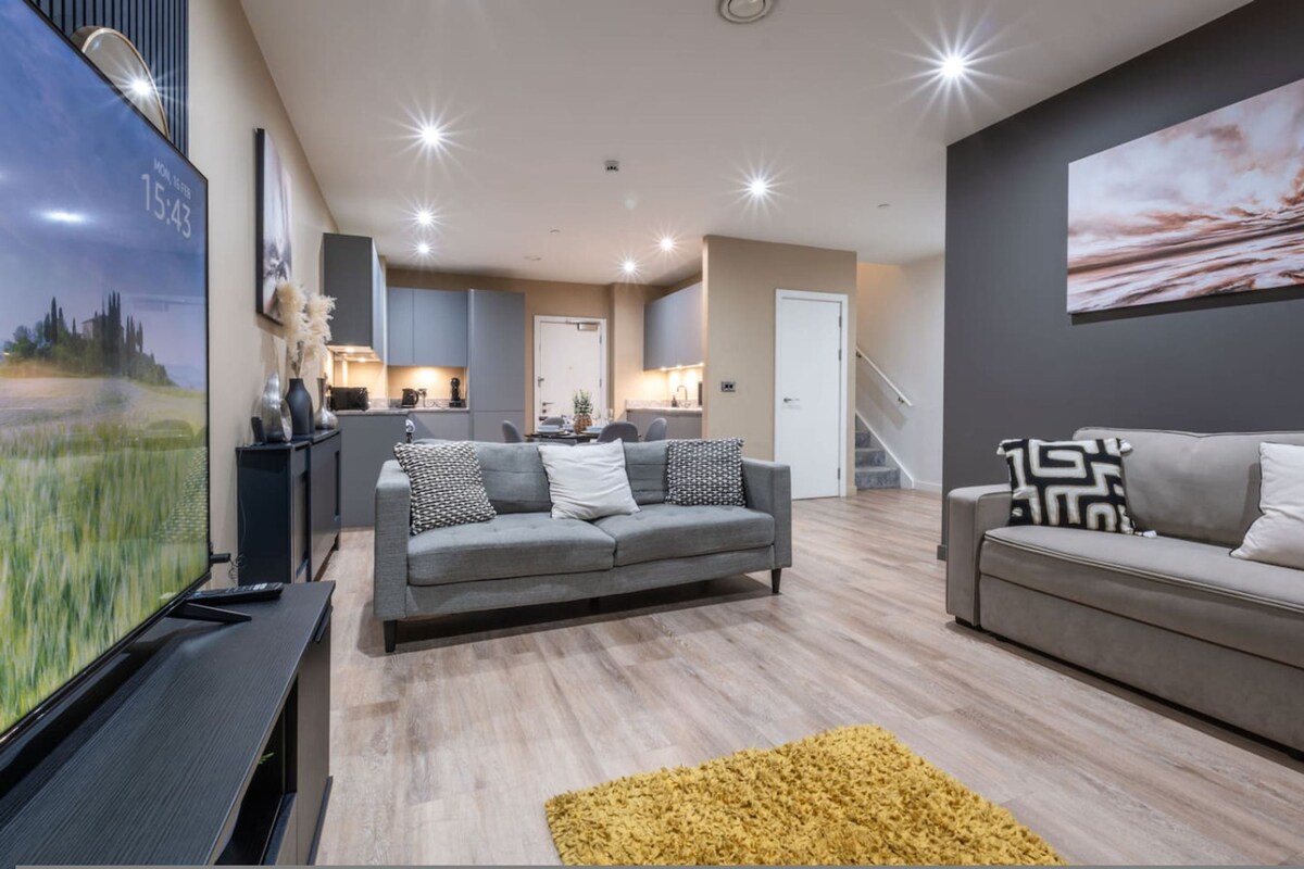 A modern living room with a grey sofa, a yellow rug, and a flat-screen TV on a stand.