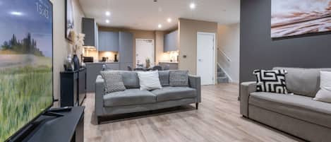 A modern living room with a grey sofa, a yellow rug, and a flat-screen TV on a stand.