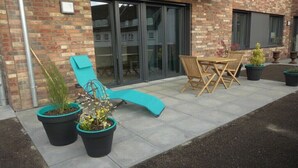 A patio area with a sun lounger, a table with chairs, and potted plants. - Holiday apartment Husumer Wattwurm (Husum)