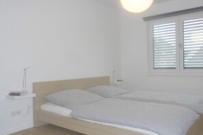 Un letto singolo con testiera in legno, un comodino con una lampada e una finestra con persiane.