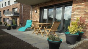 A residential building with a patio area featuring outdoor furniture, a slide, and potted plants. - Holiday apartment Husumer Wattwurm (Husum)