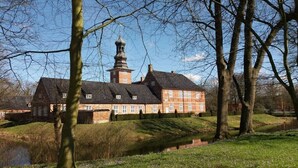 A large, historic building with a prominent tower, surrounded by trees and a small body of water. - Holiday apartment Husumer Wattwurm (Husum)
