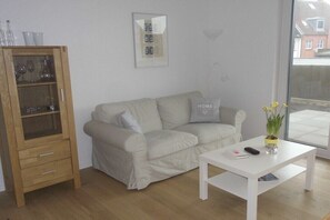 Ein Wohnzimmer mit einem weißen Sofa, einem Holzschrank, einem weißen Tisch und einem Fenster mit Blick.