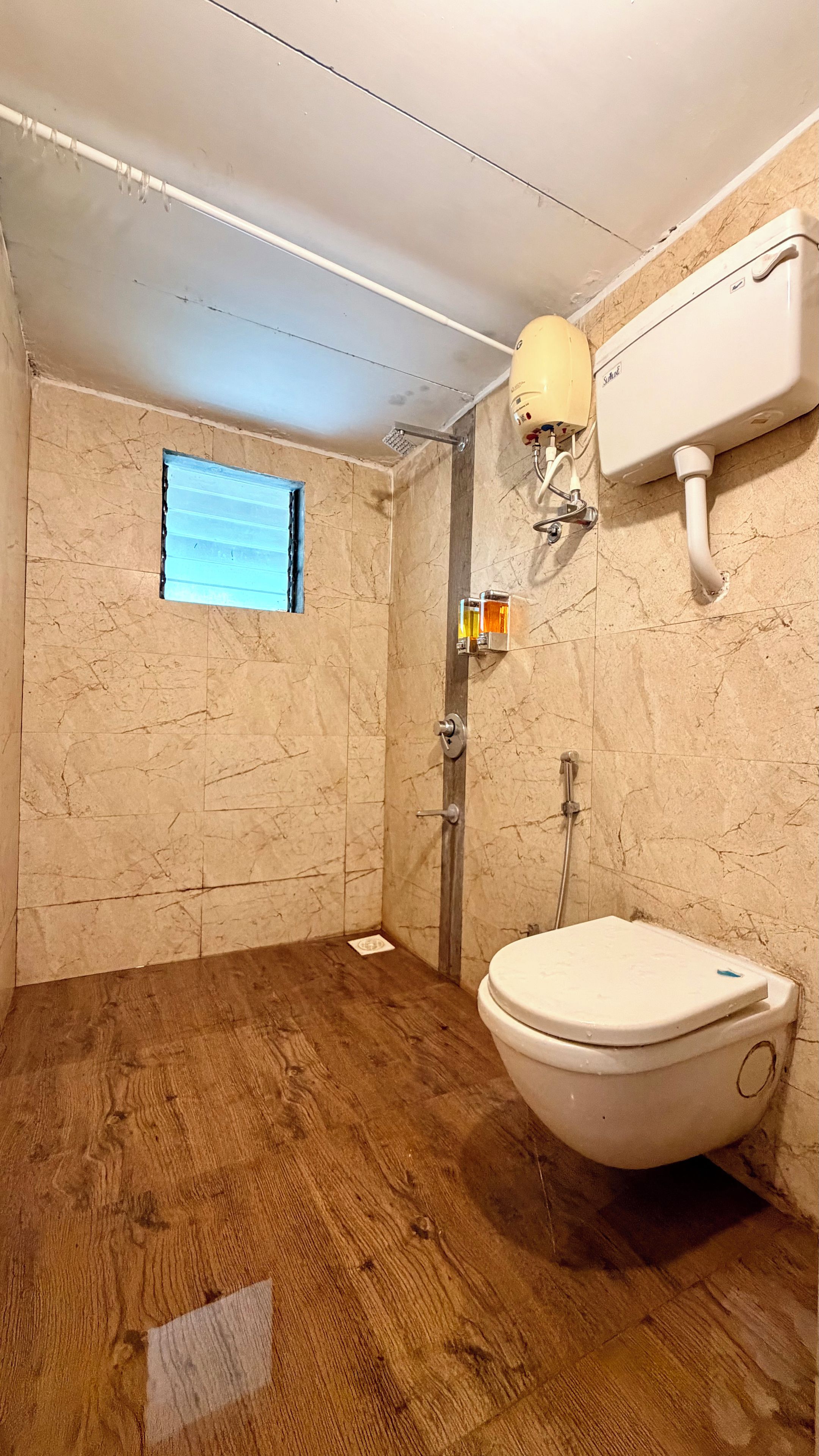 A bathroom with a wooden floor, a toilet, a shower, and a window.