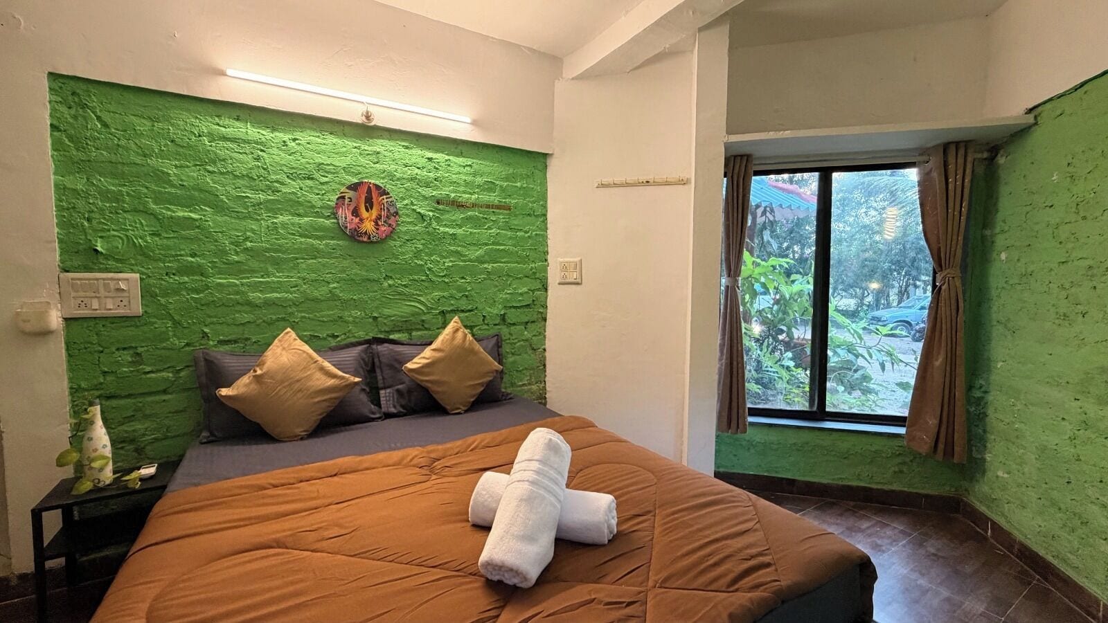 A bedroom with a green textured wall, a bed with brown bedding, and a window with curtains.