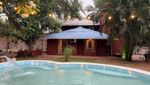 Una piscina con fuente, rodeada por un edificio de fachada roja y techo de metal corrugado.