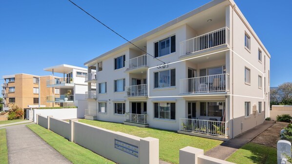 A multi-story residential building with balconies, a paved driveway, and a well-maintained lawn. - Star Lodge unit 6 Bulcock Beach QLD (Caloundra)