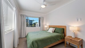 A bedroom with a bed, bedside lamps, a window with curtains, and a ceiling fan. - Star Lodge unit 6 Bulcock Beach QLD (Caloundra)