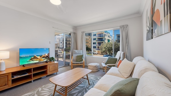 Una sala de estar moderna con televisor, zona de estar y vista de la ciudad a través de amplias ventanas.