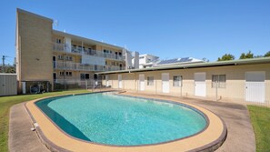 A swimming pool with a curved edge, surrounded by a fenced area, and adjacent to a multi-story building with balconies. - Star Lodge unit 6 Bulcock Beach QLD (Caloundra)