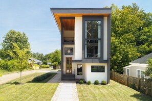 Ein modernes, zweistöckiges Haus mit flachem Dach, großen Fenstern und einer gut sichtbaren Eingangstür.