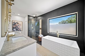 Ein modernes Badezimmer mit großem Fenster, einer freistehenden Badewanne und einer Marmorarbeitsplatte.