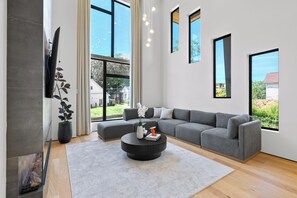 Ein modernes Wohnzimmer mit einem grauen Sofa, einem runden Couchtisch und einem großen Fenster mit Blick ins Freie.