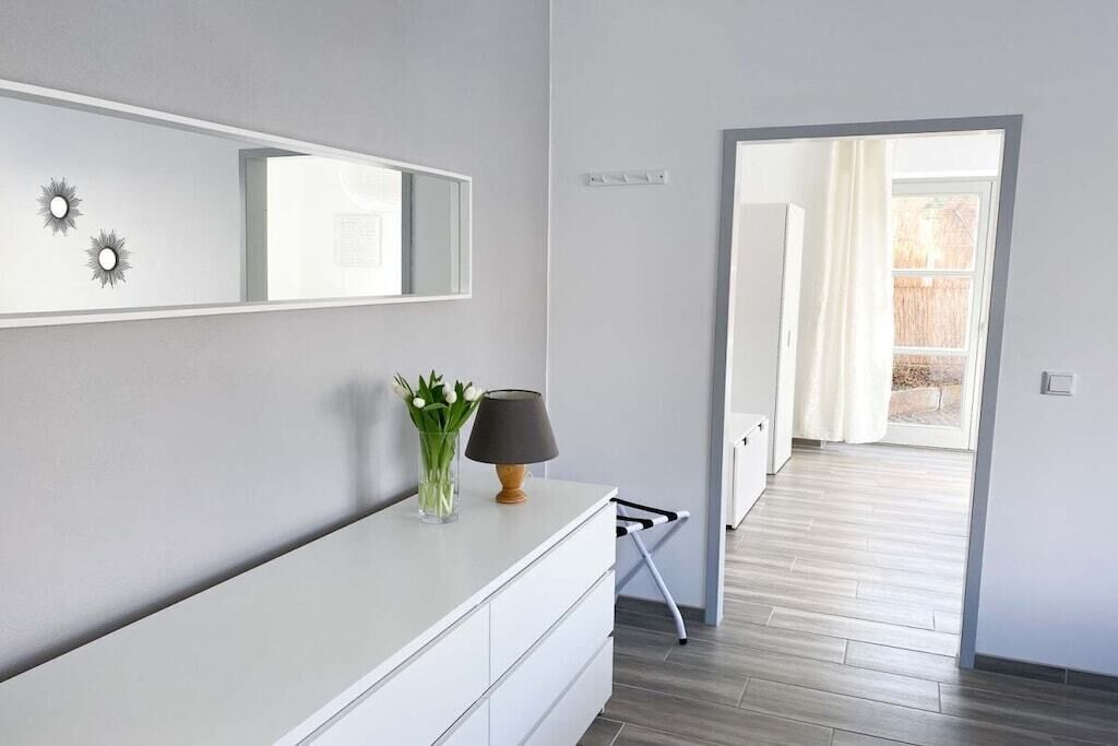Ein modernes Badezimmer mit einem weißen Waschtisch, einem Spiegel und einer Vase mit Blumen.