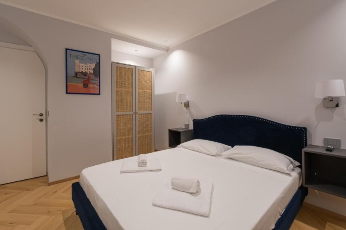Ein Hotelzimmer mit einem Bett, einem Nachttisch, einer Wandlampe, einer Tür und einem gerahmten Bild an der Wand.