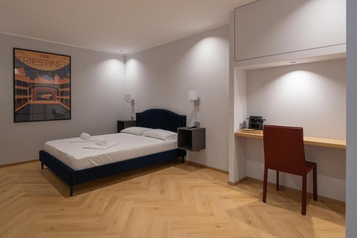 Ein modernes Schlafzimmer mit Bett, Nachttisch, Lampe und Schreibtisch mit Stuhl.