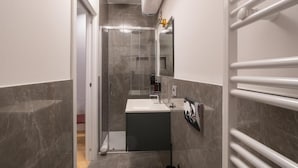 A modern bathroom with a glass shower enclosure, a sink, and a towel rack. - 23 SUITES (TRIESTE)