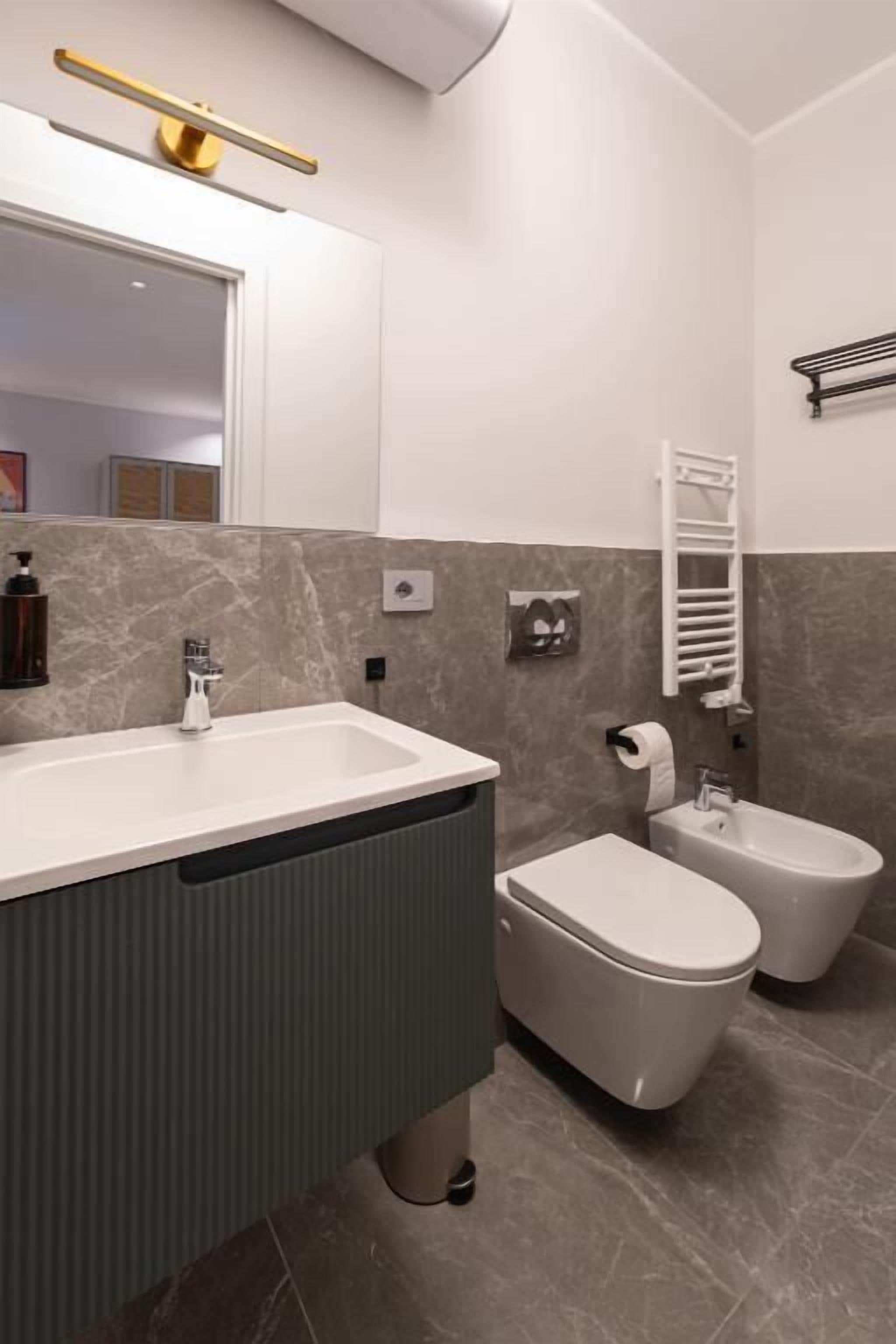 A modern bathroom with a sink, toilet, bidet, and towel rack.