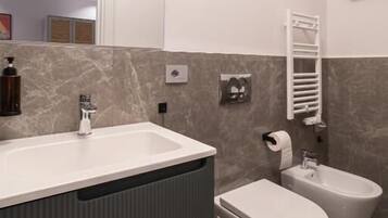 A modern bathroom with a sink, toilet, bidet, and towel rack.