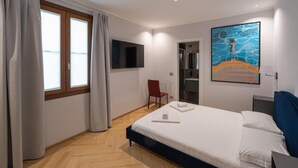 A hotel room with a bed, a TV mounted on the wall, a shower area, and a painting on the wall. - 23 SUITES (TRIESTE)