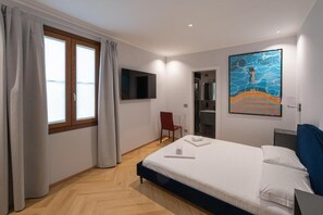 Ein Hotelzimmer mit Bett, einem an der Wand montierten Fernseher, einer Duschkabine und einem Bild an der Wand.